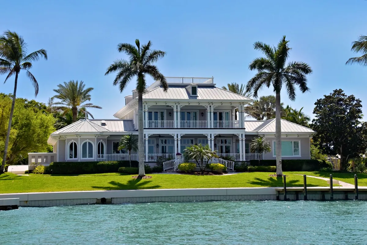 Two-story Florida waterfront home with wraparound porches, large windows and royal palms on a green lawn